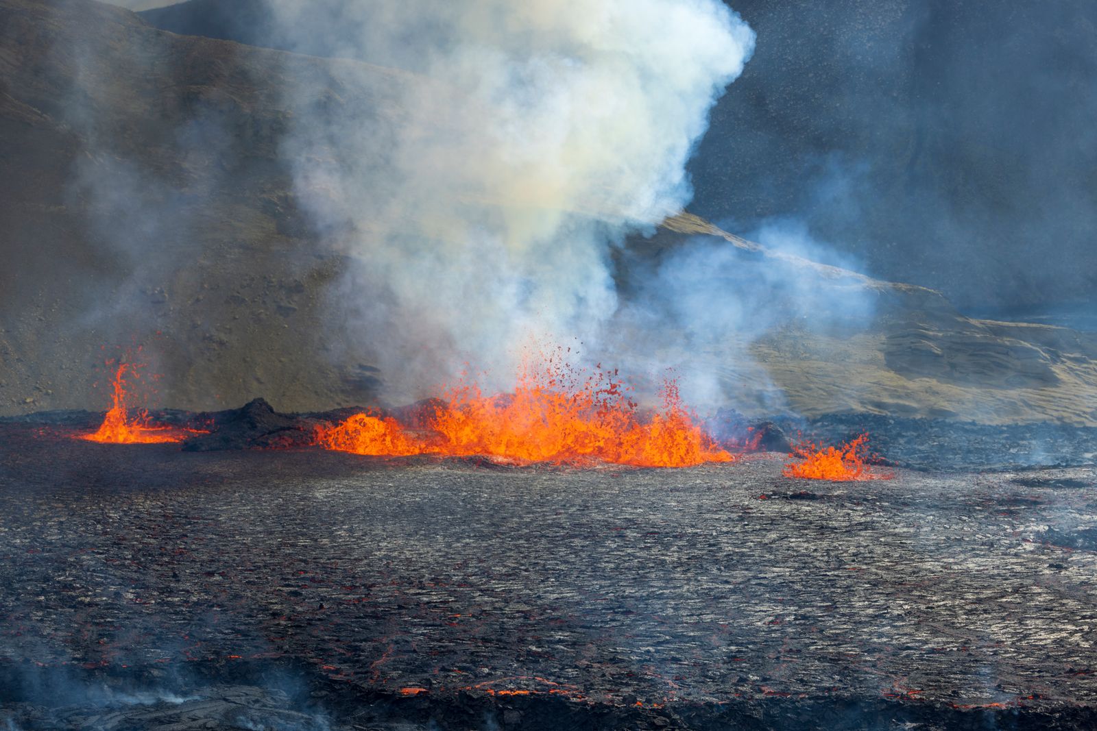 Lava flowing across the ground as volcanic smoke rises